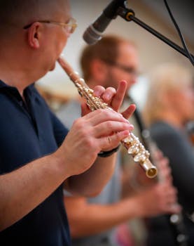 Close-up of a flute player with a microphone, performing in an orchestra.
