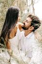 Bearded man with young cheerful woman smiling and hugging white wearing in branches in blurred landscape