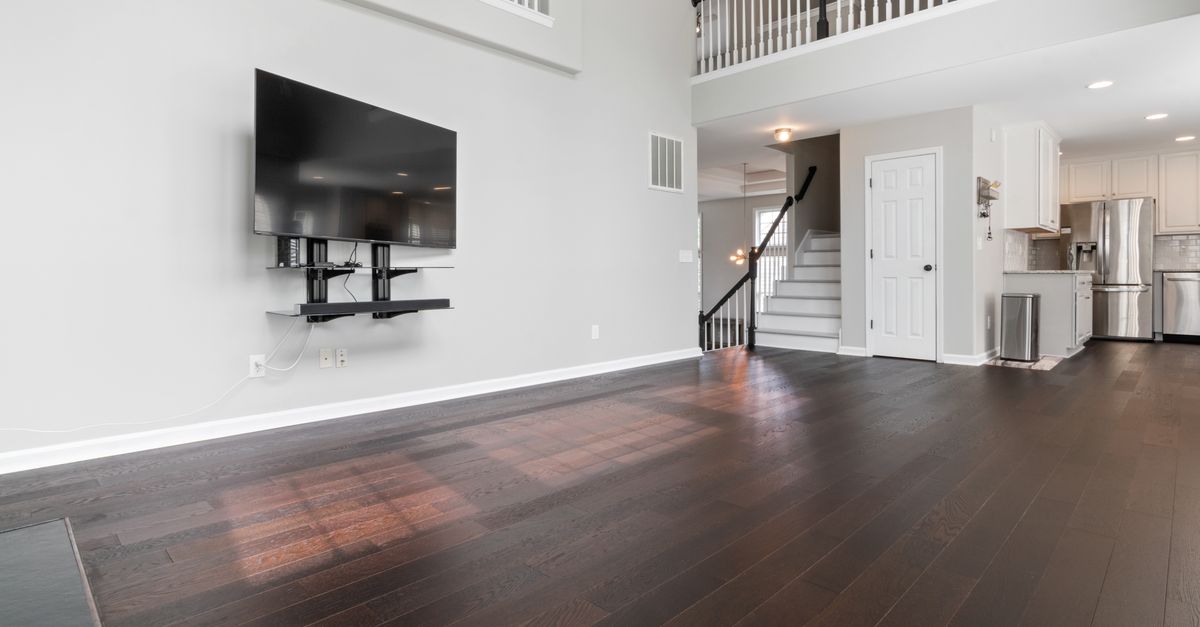 Spacious modern living room with dark wood flooring and a mounted TV, highlighting minimalist design.