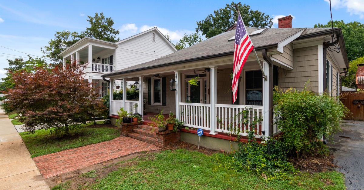 Quaint American bungalow with flag and lush garden under a blue sky.