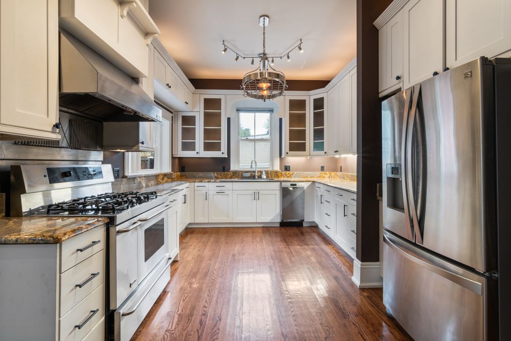 Modern white kitchen featuring wooden floors, stainless steel appliances, and granite countertops