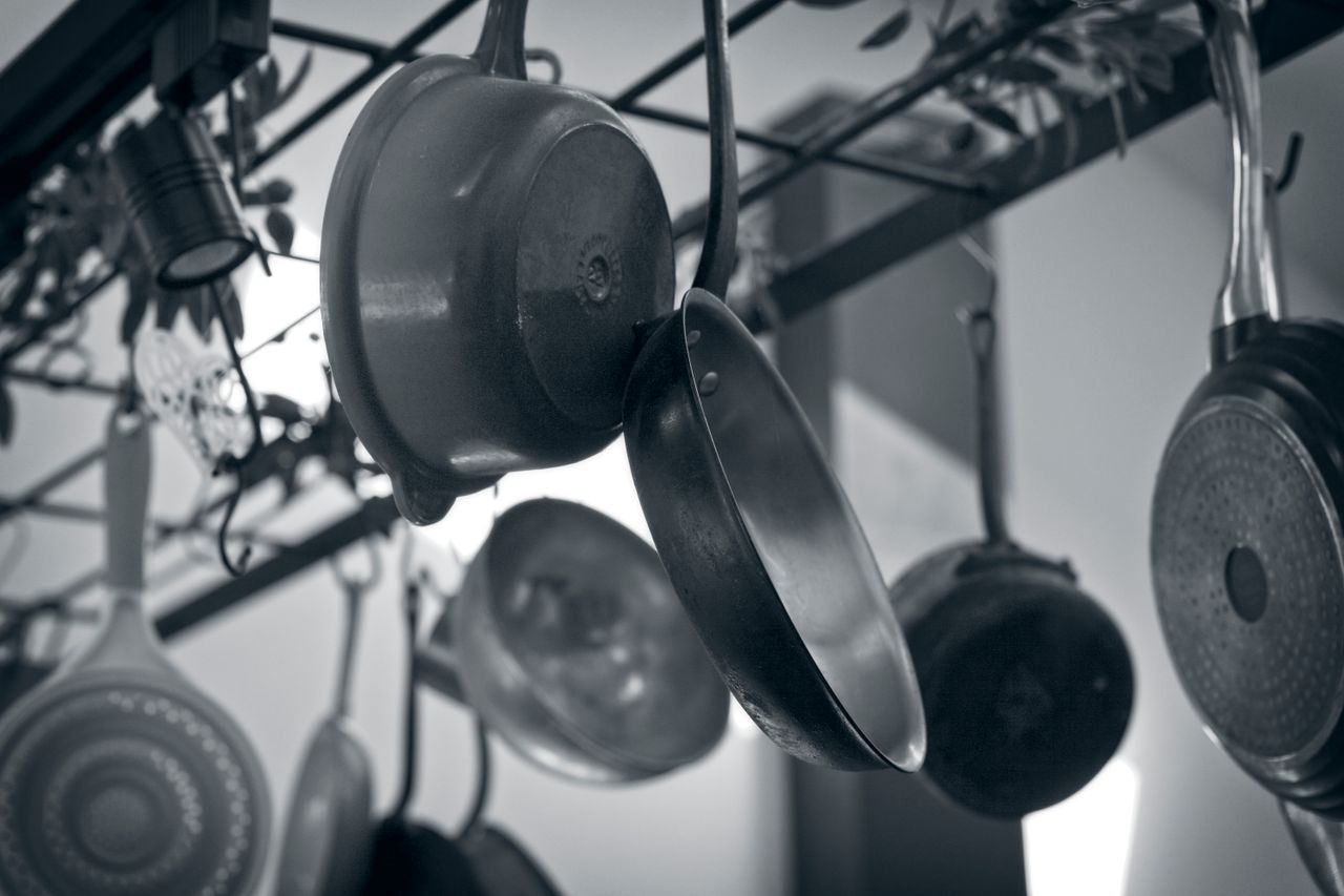 Black-and-white photo of pots and pans hanging from an overhead kitchen rack