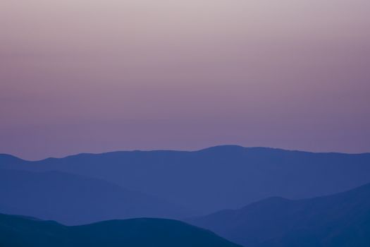 Breathtaking view of sundown sky with pink color over foggy mountain peaks in evening time in nature in countryside outside