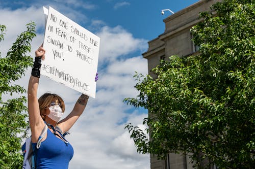 Low angle of anonymous female in protective mask raising placard with inscription motivated to protect people during demonstration in street