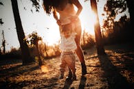 Crop faceless woman holding hands of adorable baby and walking in grassy park