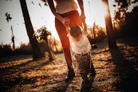 Crop woman holding hands and leading little boy in casual clothes at sunset