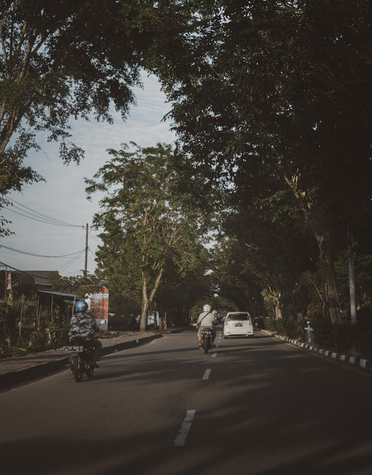 People Riding On Scooters On An Asphalt Road 