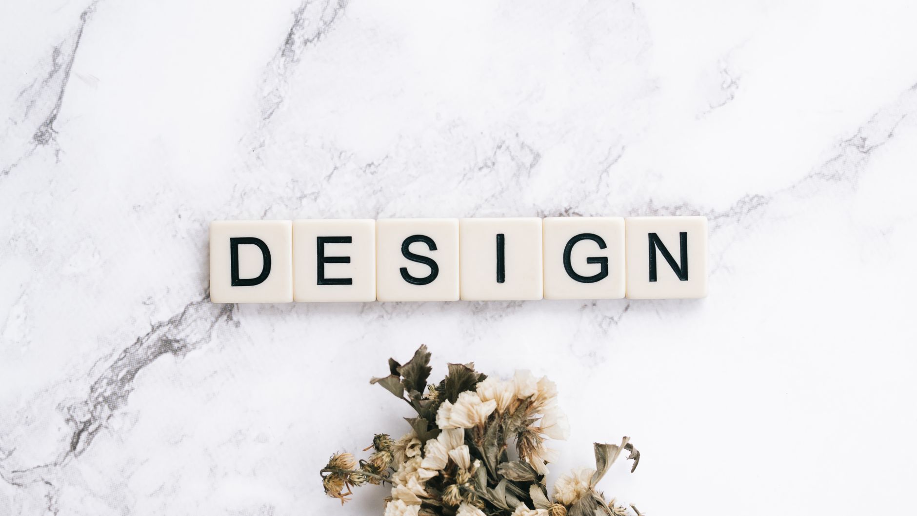 Close-up of Scrabble tiles spelling 'design' on marble with flowers.