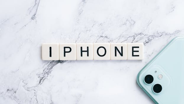 Flatlay of scrabble tiles spelling iPhone next to a smartphone on a marble surface.