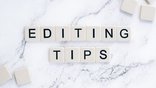 Free Scrabble tiles spell out 'Editing Tips' on a marble background, perfect for editorial guides. Stock Photo