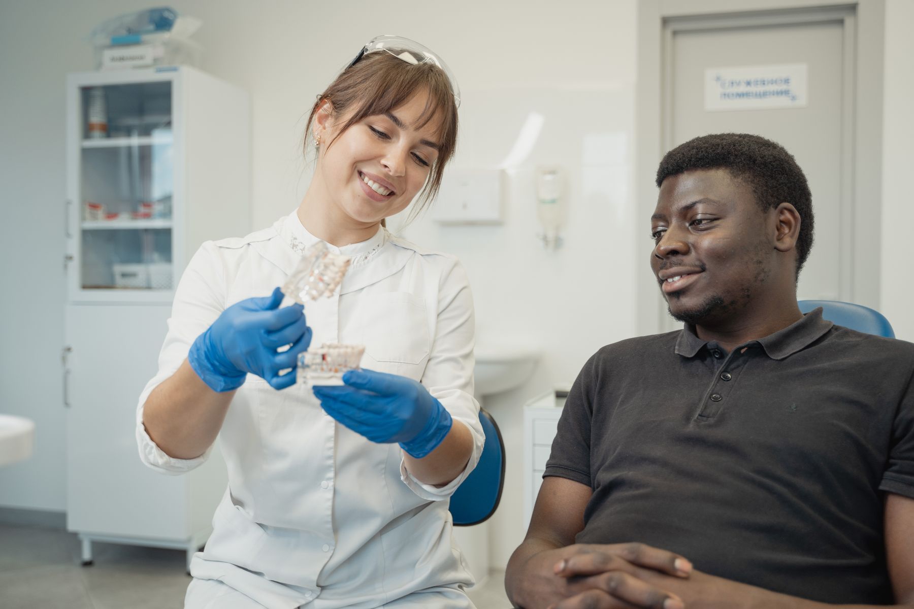 Smiling dentist explaining a dental model to a prospective cosmetic dentistry patient in a modern private dental clinic