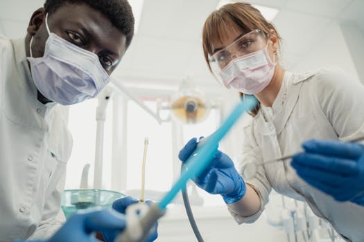 Two dentists in protective gear examining a patient with dental tools in a clinic.