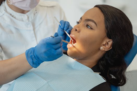 A female patient undergoing a dental checkup by a healthcare professional wearing gloves and a facemask.