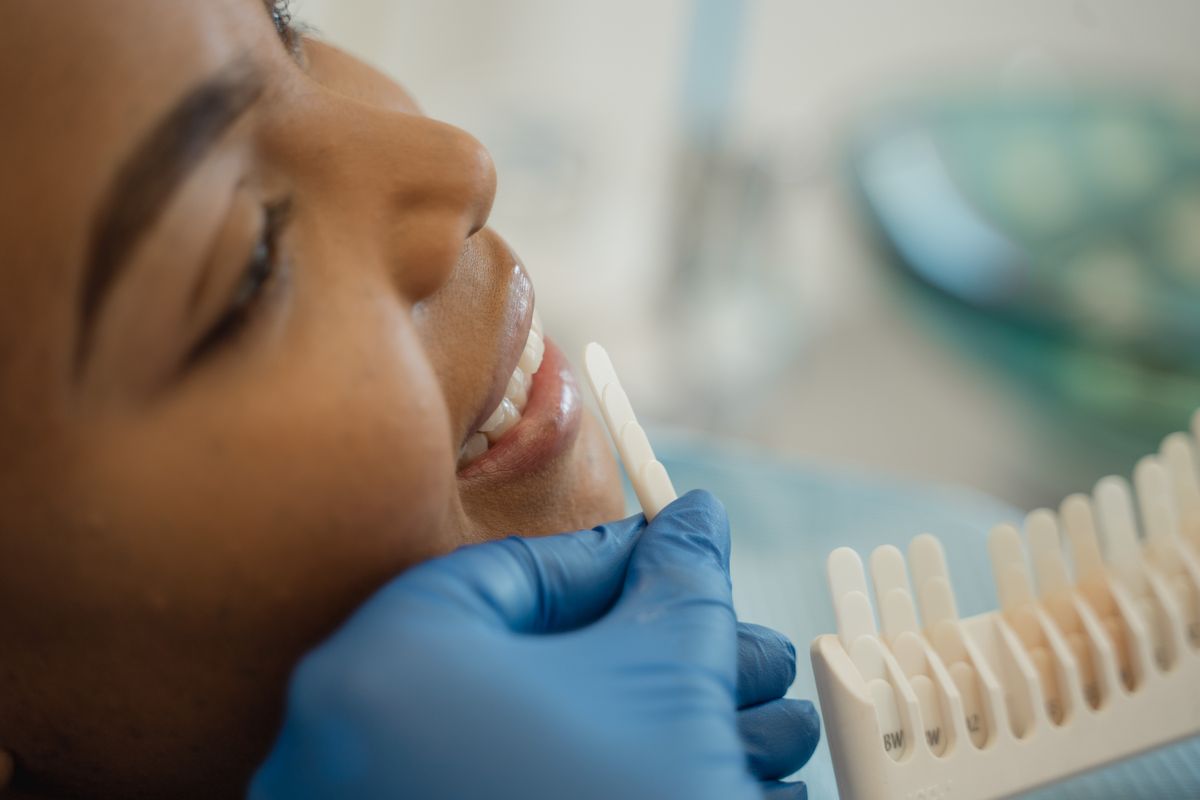 Dentist matching a shade guide to a woman's natural teeth before cosmetic treatment