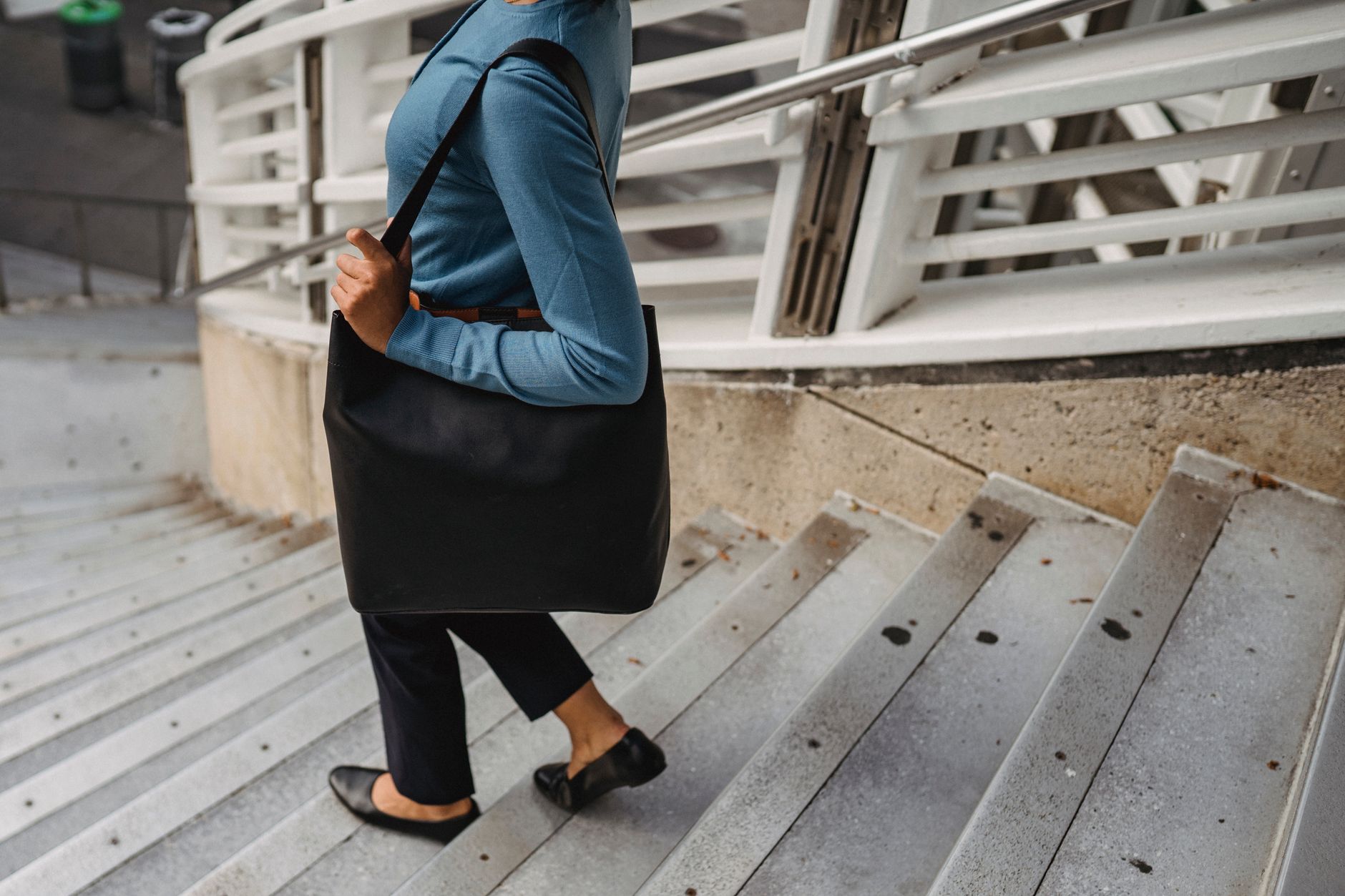 From above of unrecognizable African American female in casual outfit with bag walking downstairs near railing on street in city