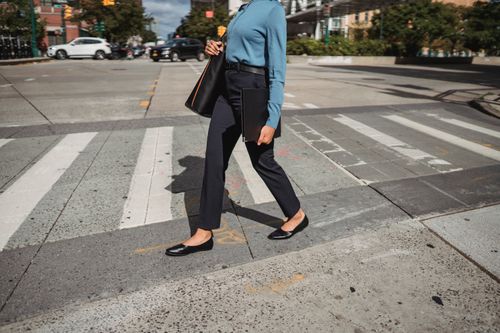 Free Unrecognizable female in casual wear with black bag walking on pedestrian crossing on sunny street in city with buildings on background Stock Photo