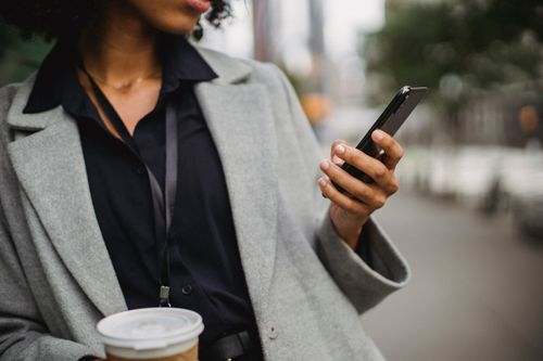 Free Unrecognizable ethnic female in formal clothes browsing cellphone while standing in city on blurred street with cup of drink during break Stock Photo