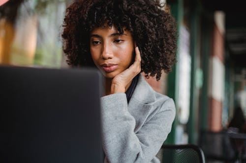 Free Crop attentive well dressed black female executive with Afro hairstyle touching face while watching netbook Stock Photo