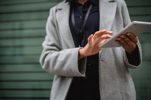 A woman in a gray coat uses a tablet against a blurred background. Modern business concept.