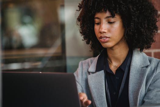 Focused woman using a laptop in an indoor setting, showcasing professionalism and concentration.