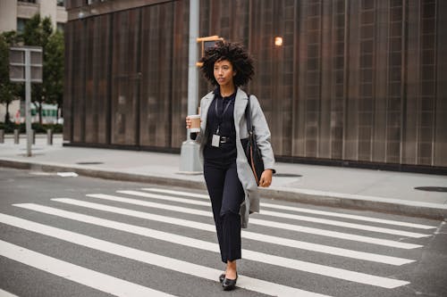 Stylish black office worker with takeaway coffee strolling on crosswalk