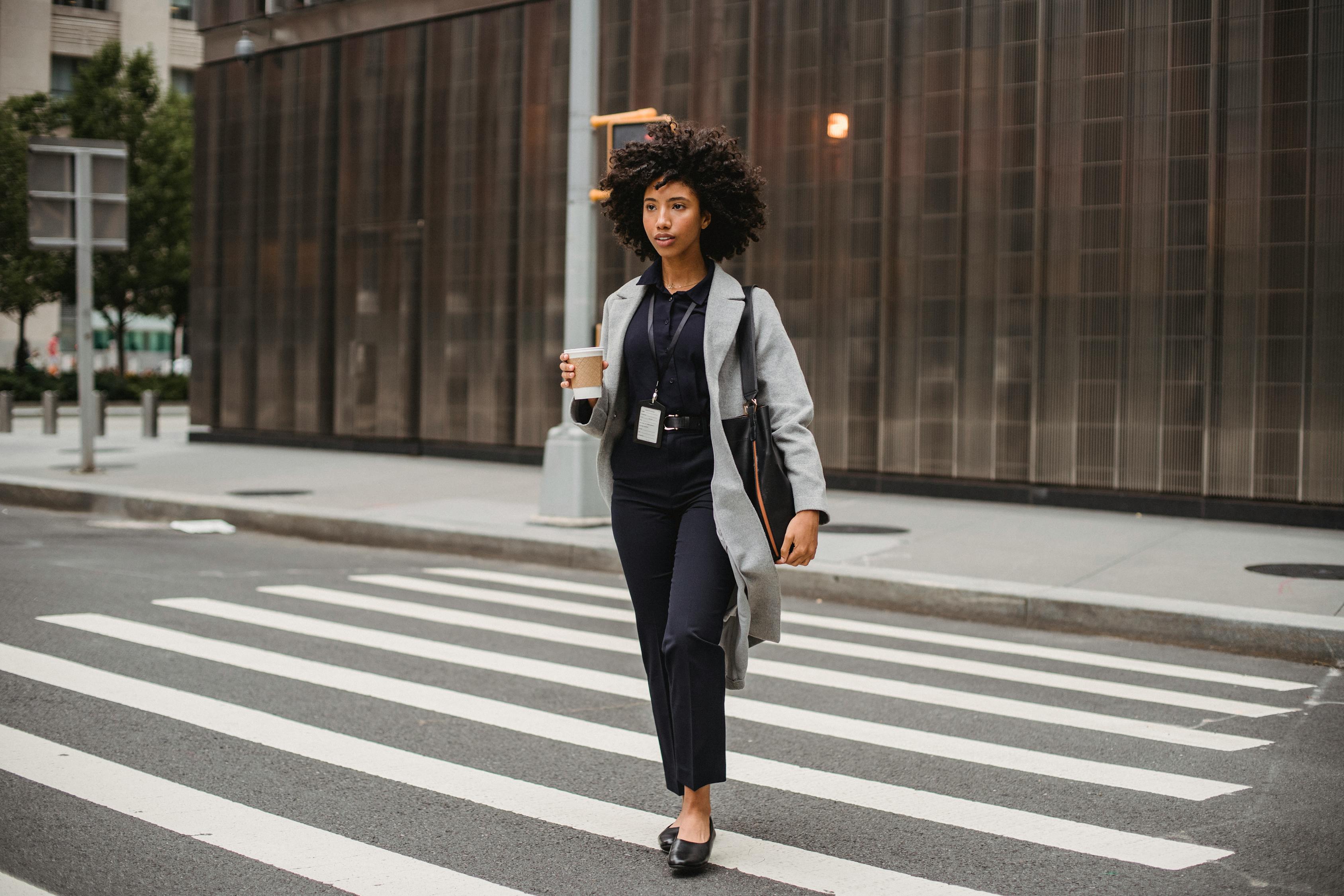 Stylish black office worker with takeaway coffee strolling on crosswalk ...