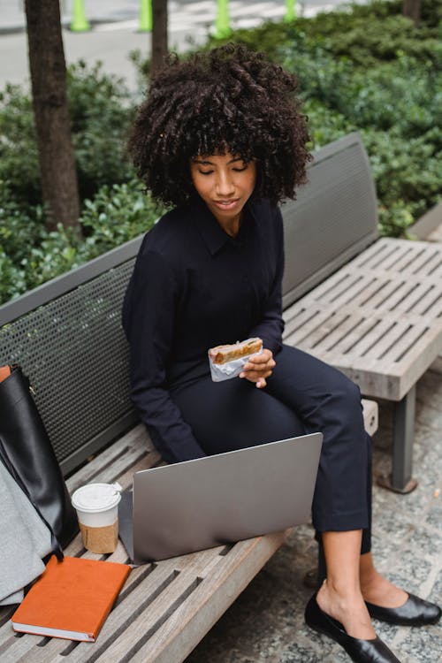 Free Black businesswoman with puff working on laptop on street bench Stock Photo