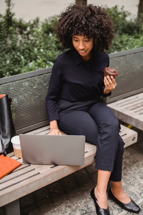 Businesswoman with laptop and muffin on bench