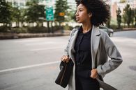 Confident African American female in trendy outfit holding hand in pocket while standing on pavement street in windy weather and looking away