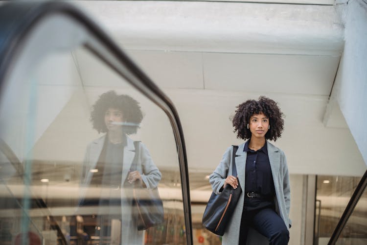 Black Woman Standing On Escalator In Mall