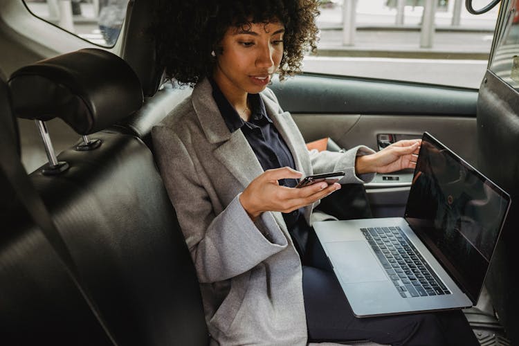 Black Woman With Smartphone In Backseat Of Car