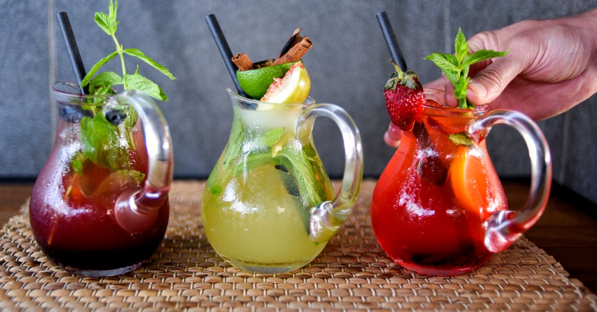 Colorful fruit cocktails served in glass mugs with fresh garnishes.