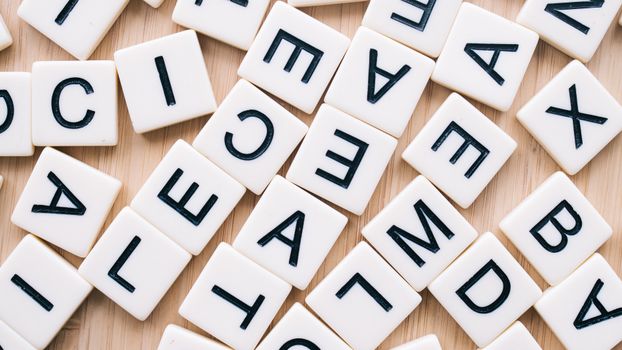 A close-up of scattered letter tiles on a wooden surface, captured from above.