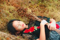 一幅平静的肖像：一个女人穿着花裙躺在草地上，手拿干花