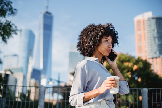 A young woman talks on her smartphone while holding a coffee cup in a vibrant city environment.