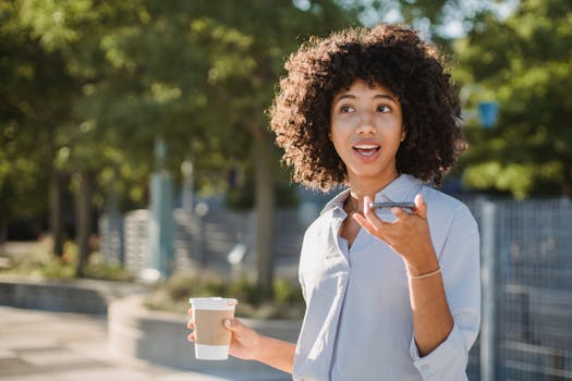 African American woman talking on phone, holding coffee outdoors on a sunny day.