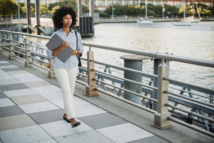 Photograph Of A Woman Walking While Holding Her Laptop