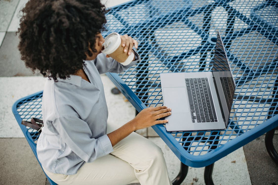 Photo of a Woman Drinking Coffee while Working on Her Laptop