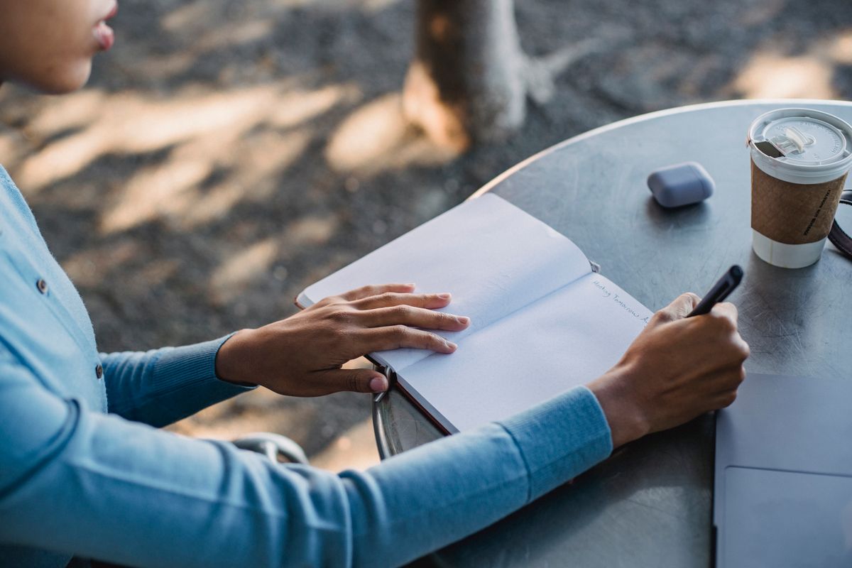 A person writing in an open journal at a café table, coffee cup nearby.