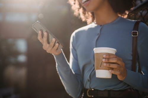 Free Photo of a Woman Holding a Cup of Coffee and Her Cell Phone Stock Photo