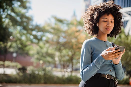 An adult woman with curly hair text messaging on her smartphone outdoors.