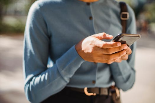 Close-up of a person using a smartphone outdoors, focusing on hands and mobile device.