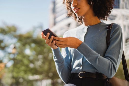 A young woman in a blue sweater using a smartphone outdoors in the city.