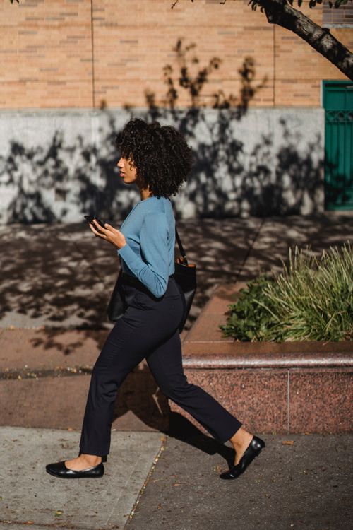 Free African American woman with afro hair walking outside while holding a mobile phone. Stock Photo