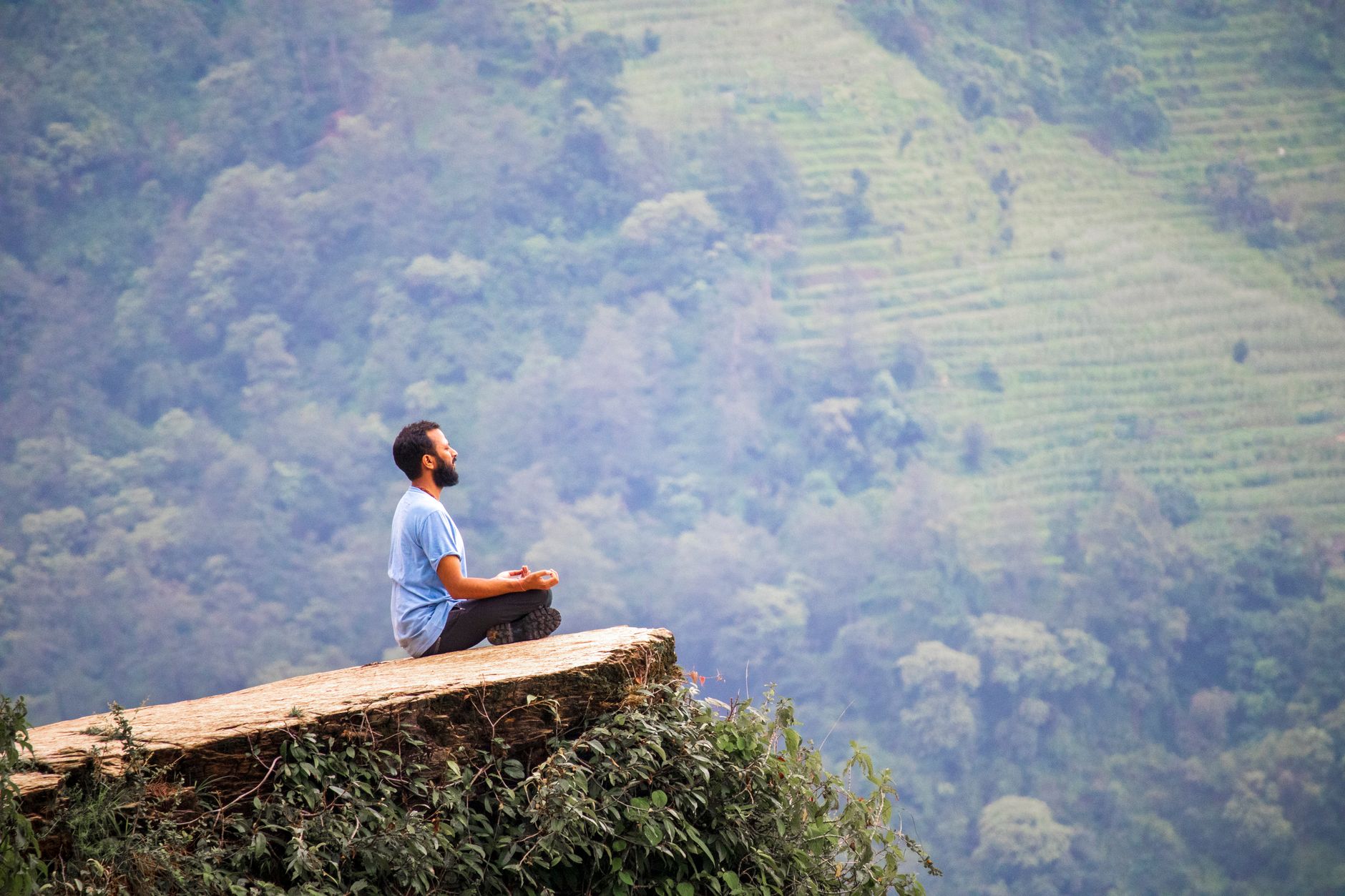 biohacking beginners guide — Man meditating on a cliff with lush green mountains in Ghandruk, Nepal.