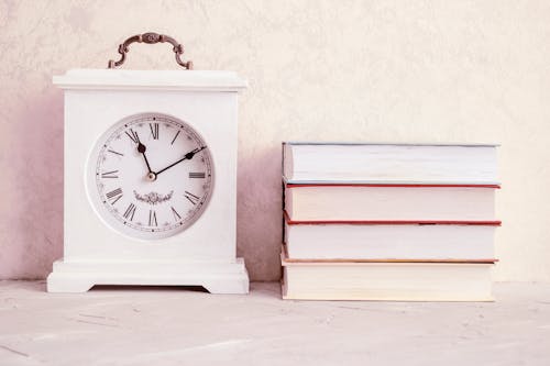 Photograph of a White Vintage Clock Beside a Stack of Books