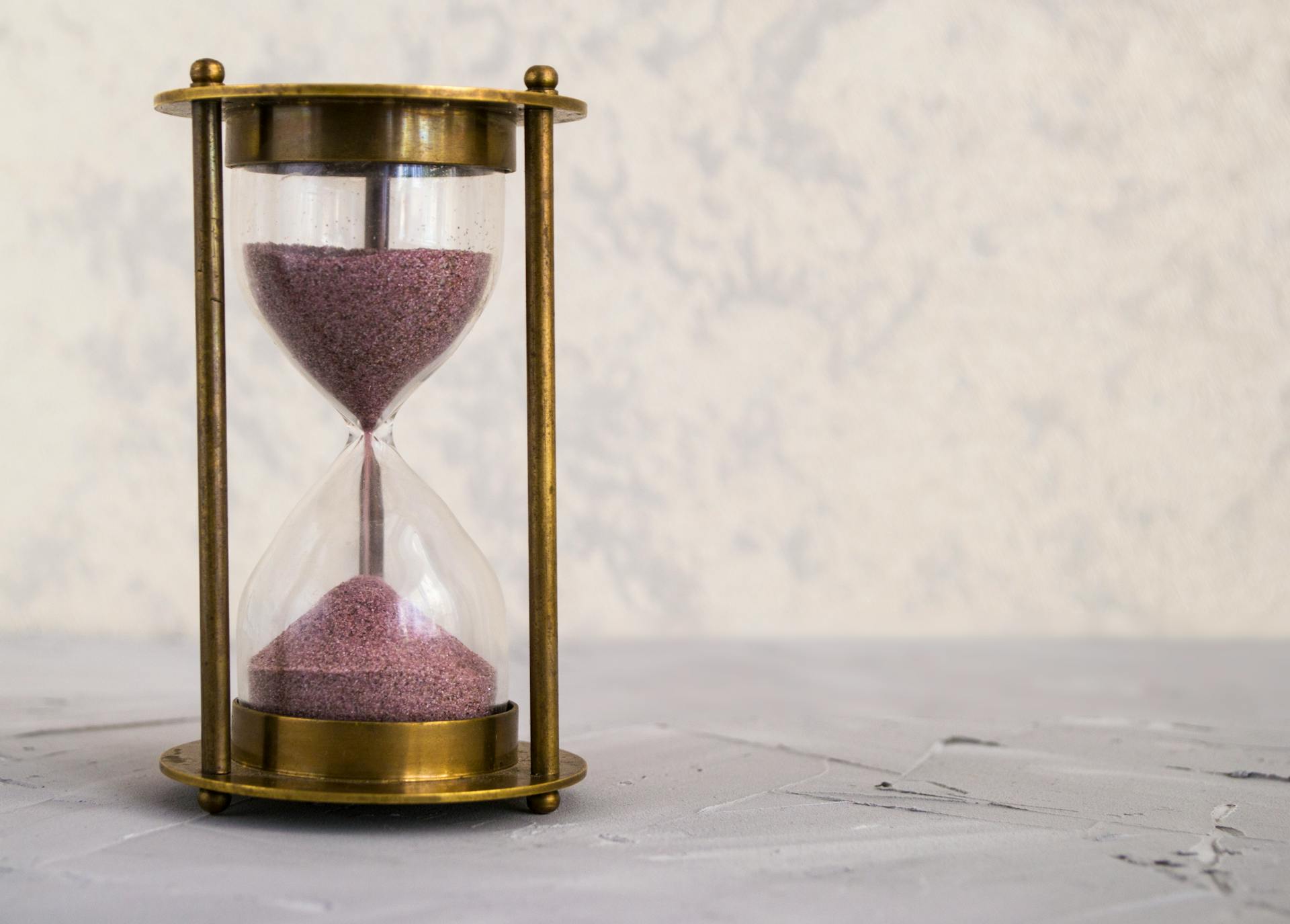 A traditional hourglass with pink sand, symbolizing time and patience on a textured surface.