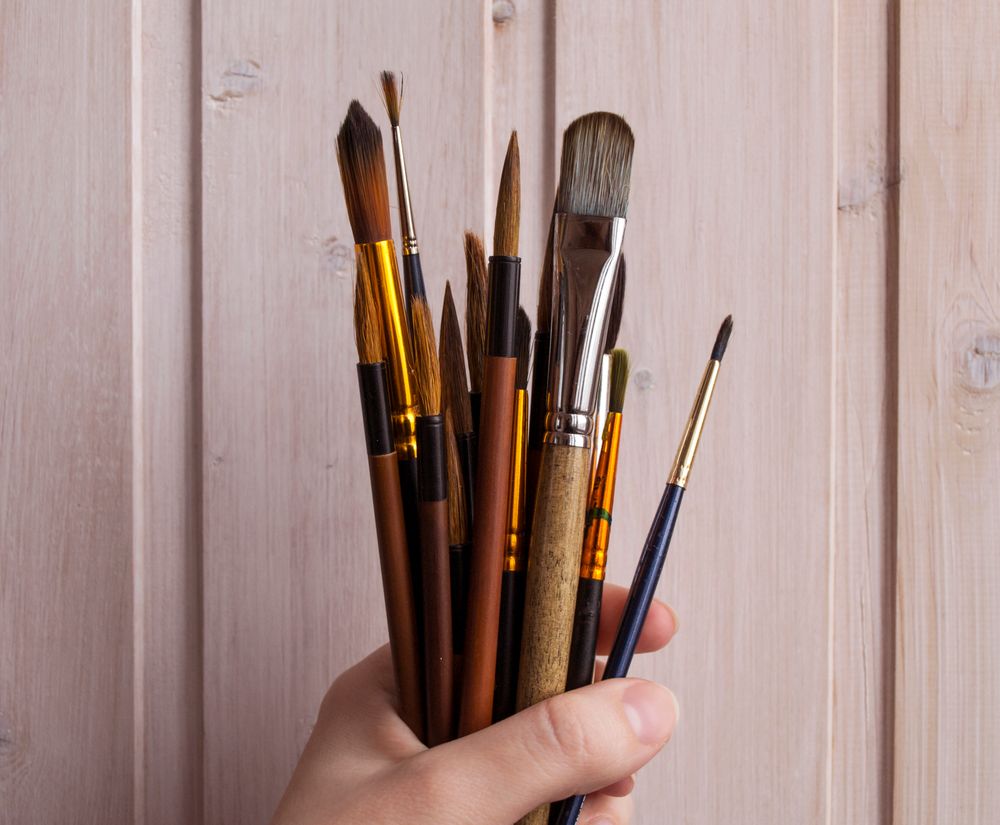 A handful of wide flat brushes held against a timber wall