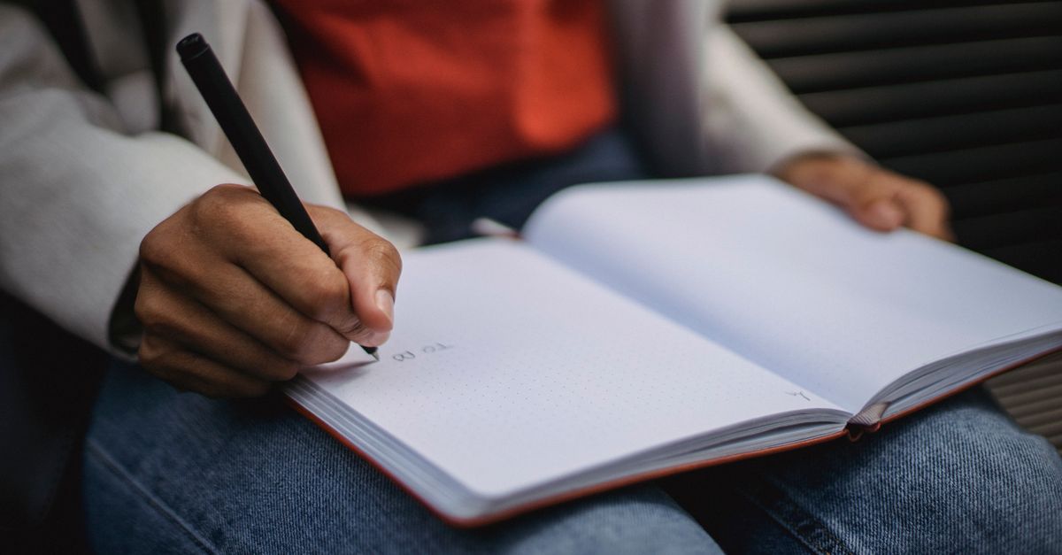 Hand holding pen writing in an open notebook, indicating study or journaling.