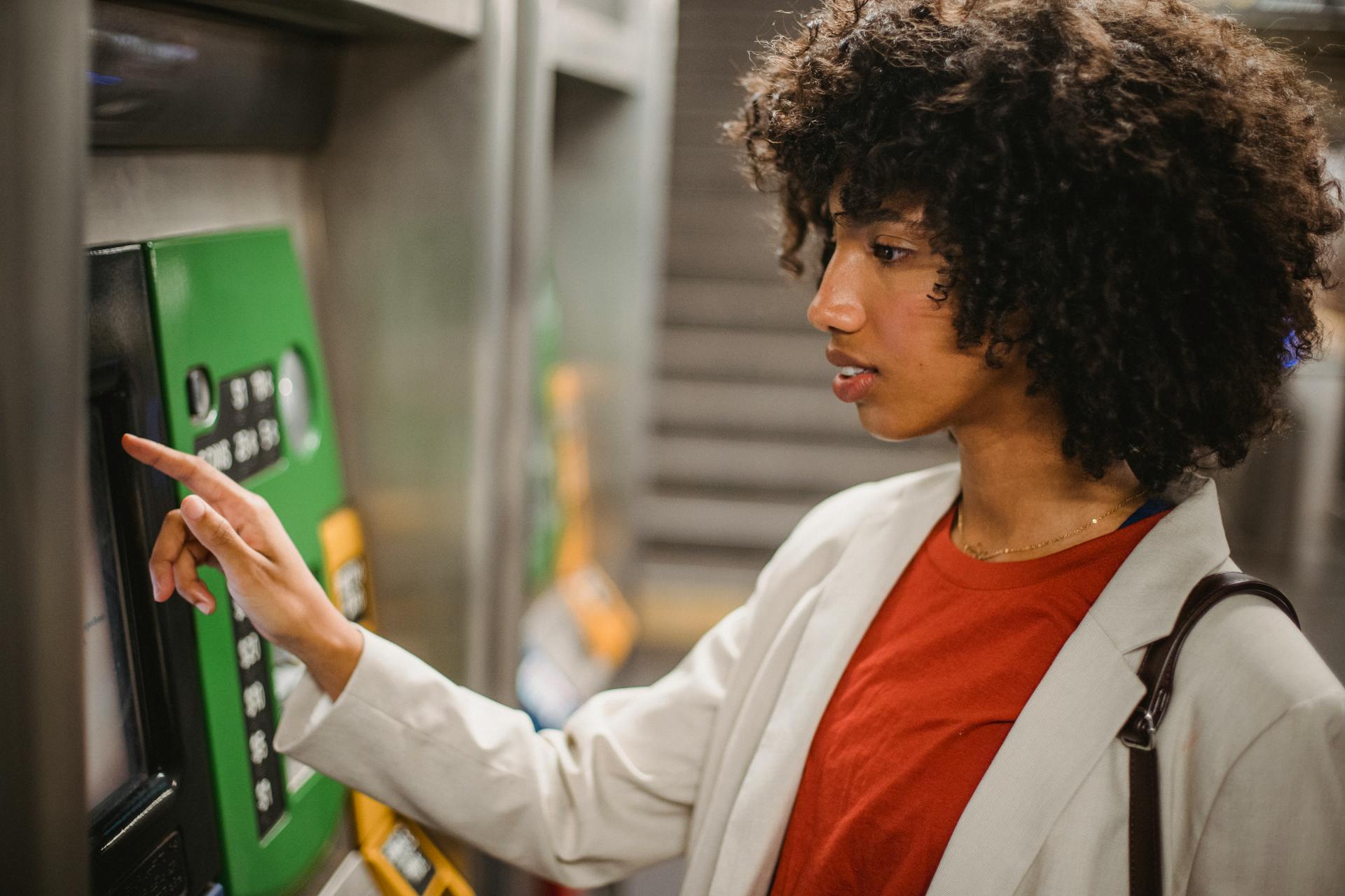 African American woman with curly hair using an ATM machine indoors.